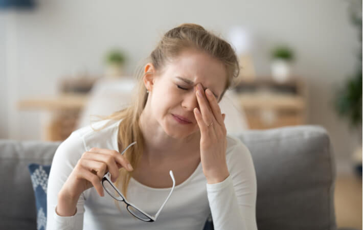 A woman in visible discomfort rubs her eyes with her left hand.