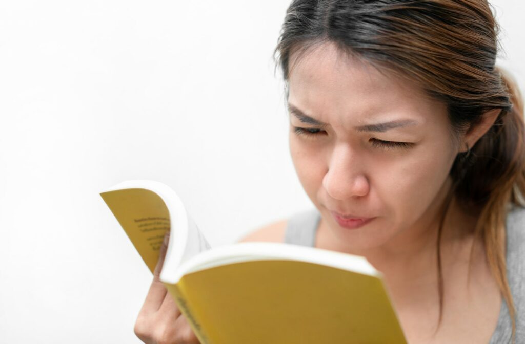 A young woman squinting while reading a book