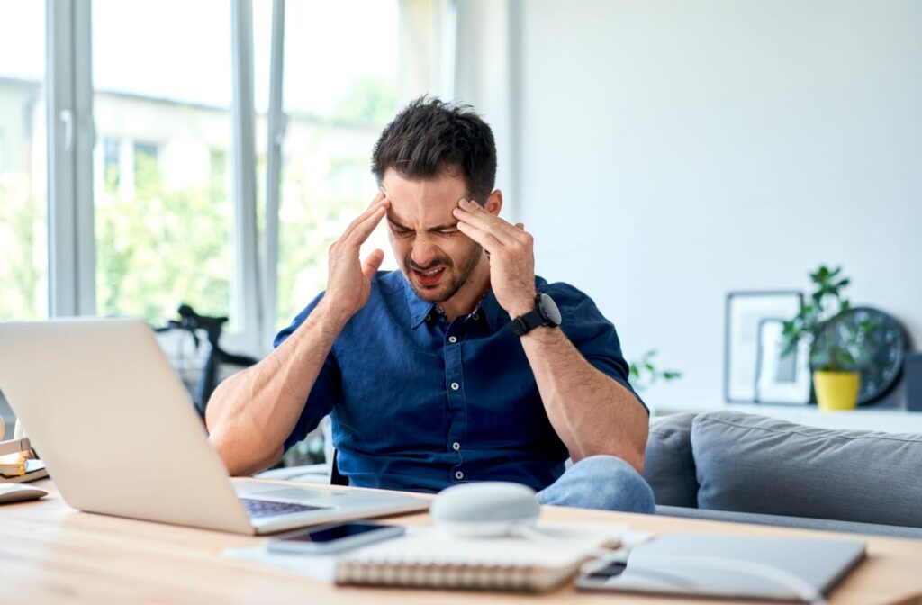 A young man experiencing a headache in his home office