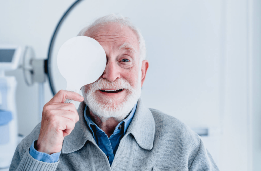 A cheerful elderly man is covering his right eye while undergoing a visual acuity examination.