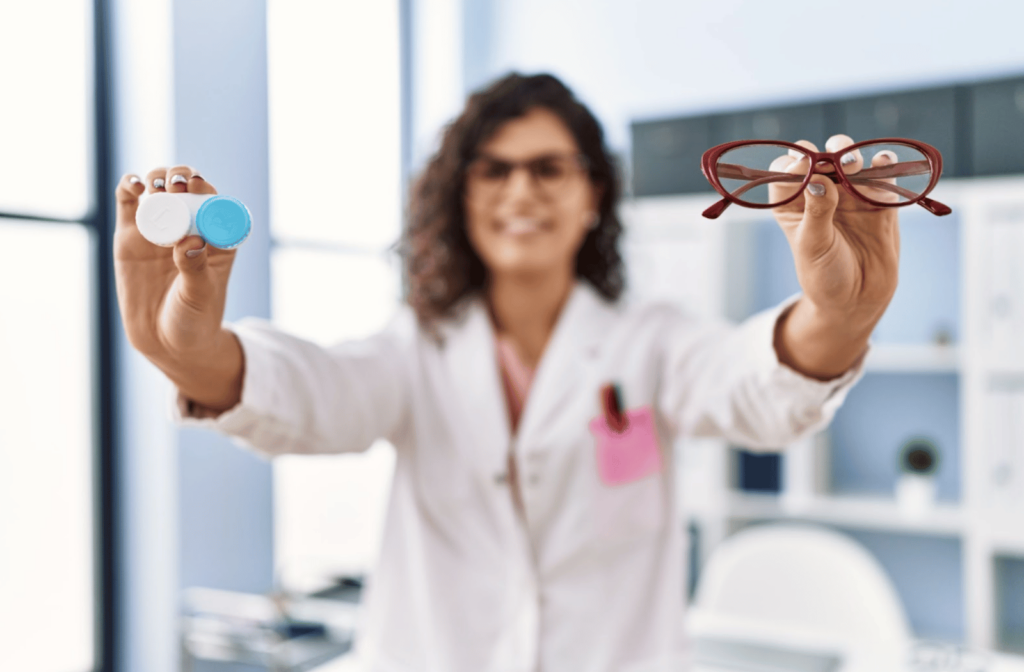An optometrist holds out a contact lens case in one hand and a pair of glasses in the other hand