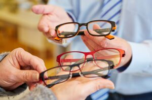 A close-up image of an older adult's hands with several pairs of glasses as an optician shows off a new pair.