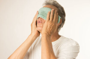 A person covering their eyes with a warm cloth to unclog their eyelid glands.