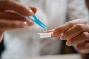 A person using tweezers to pick up a contact lens from its container.